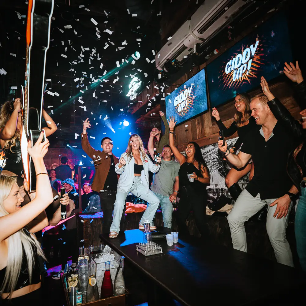 Guests dancing on the bar top under falling confetti and blue lights at Dierks Bentley's Whiskey Row