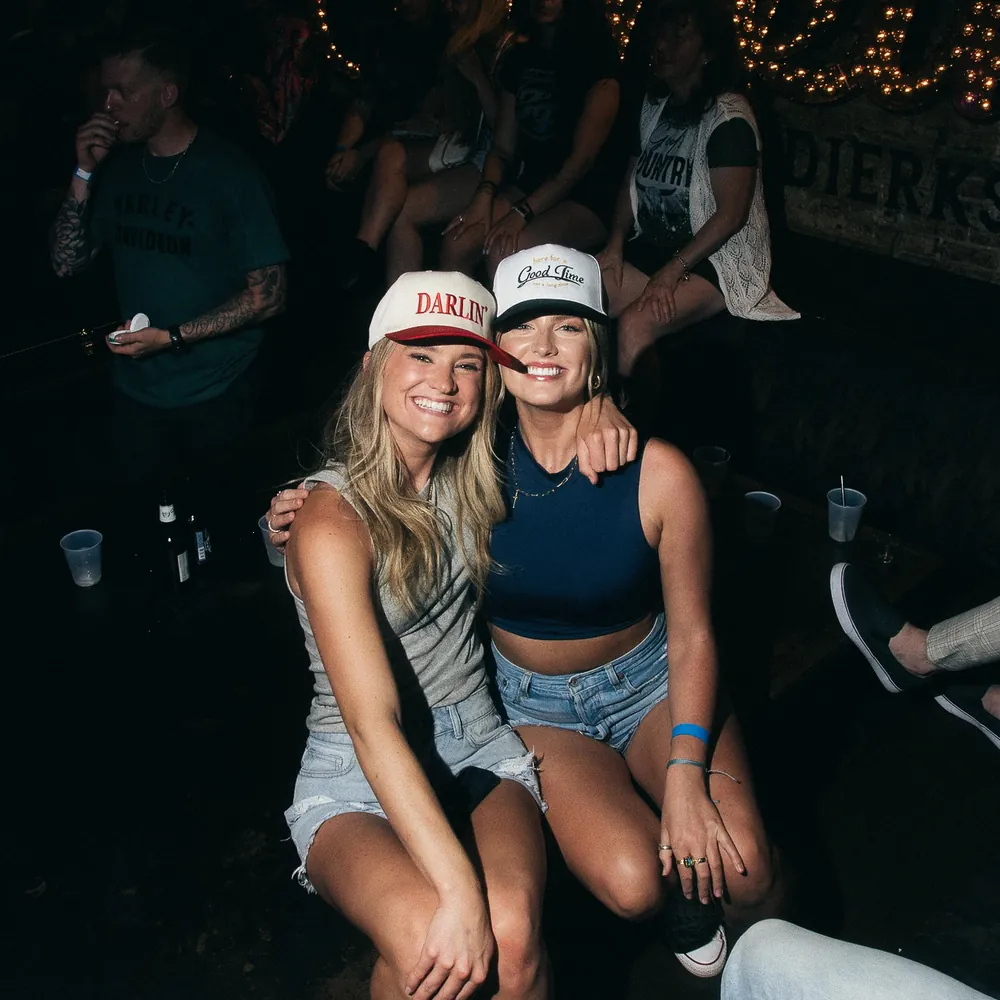 Two smiling friends in trucker hats sitting together inside the bar at Dierks Bentley's Whiskey Row