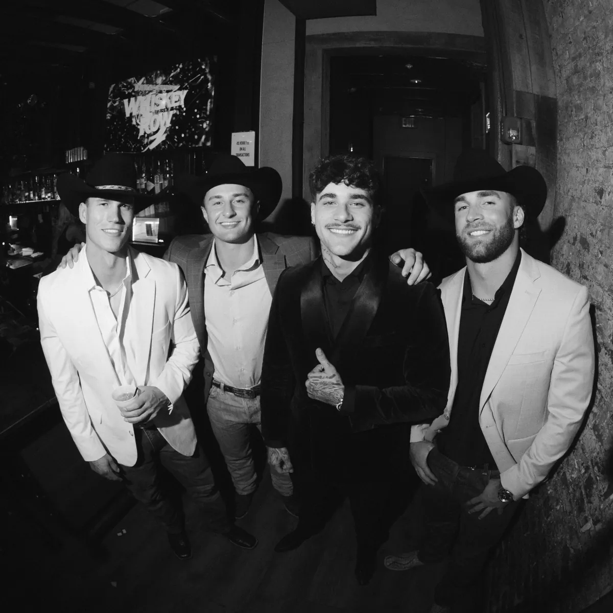 Four men dressed up in blazers and black cowboy hats smiling together at a private event at Dierks Bentley's Whiskey Row