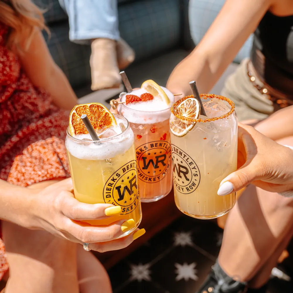 Three Whiskey Row signature cocktails garnished with citrus raised for a cheers