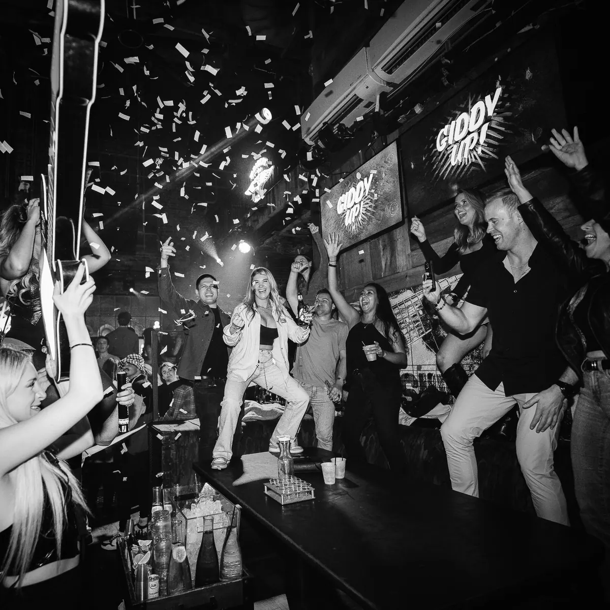 Guests celebrating at a VIP bottle service table at Dierks Bentley's Whiskey Row, dancing on the booth as confetti falls under Giddy Up signs
